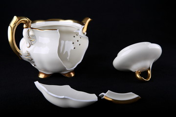 broken porcelain teapot with pieces close up on a black background