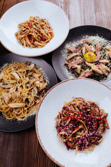 Several plates of pasta with different kinds of sauce over wooden background, top view. Concepts of Italian food.
