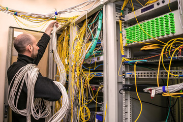 A communication specialist with hand-wound wires works in the server room. A man wrapped in cables...