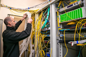 The system administrator is laying new cable communications in server racks. The man switches the...