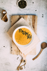 A bowl with pumpkin soup on a wooden board and a small bowl with pumpkin seeds aside