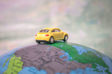 The concept of travel around the world on a passenger auto. A yellow toy car is traveling around...