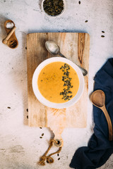 Fototapeta na wymiar A bowl with pumpkin soup on a wooden board and a blue kitchen cloth aside