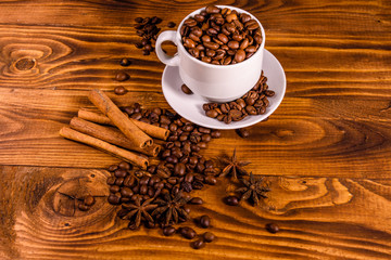 White cup filled with coffee beans, star anise and cinnamon sticks on wooden table