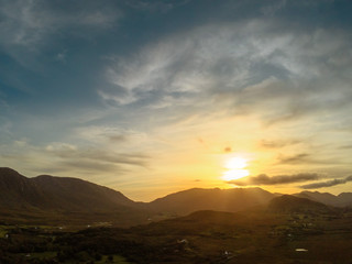 Sun set over mountains, dark and moody light, Colorful sky and sun flare, Connemara National Park, county Galway, Ireland. Aerial view.