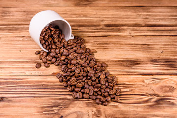 White cup and scattered coffee beans on wooden table
