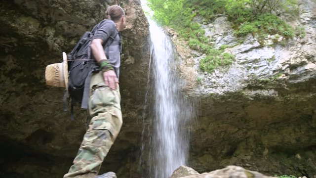Traveler climbs on stone, looking at beautiful view of waterfall. Closeup