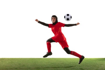 Arabian female soccer or football player isolated on white studio background. Young woman kicking the ball, training, practicing in motion and action. Concept of sport, hobby, healthy lifestyle.