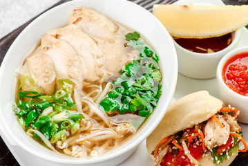 Asian noodle soup, ramen with chicken, tofu, vegetables in white plate on a dark restik tray in beautiful composition with fresh herbs on light concrete background. Close up. Top view.