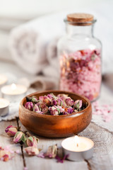 Fototapeta na wymiar Concept of spa treatment with roses. Dry flowers in a bowl, crystals of sea pink salt in bottle, candles as decor. Atmosphere of relax, anti-stress and detox prosedure. Luxury lifestyle. 