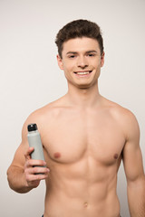 Fototapeta premium smiling shirtless man looking at camera while holding deodorant isolated on grey