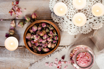 Obraz na płótnie Canvas Concept of spa treatment with roses. Dry flowers in a bowl, crystals of sea pink salt in bottle, candles as decor. Atmosphere of relax, anti-stress and detox. Luxury lifestyle. Flat lay, top view