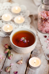 Obraz na płótnie Canvas Concept of spa treatment with roses. Herbal tea, crystals of sea pink salt in bottle, candles as decor. Atmosphere of relax, anti-stress and detox procedure. Luxury lifestyle. Wooden background
