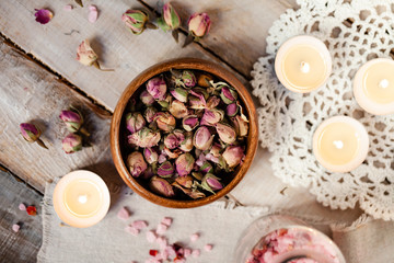 Fototapeta na wymiar Concept of spa treatment with roses. Dry flowers in a bowl, crystals of sea pink salt in bottle, candles as decor. Atmosphere of relax, anti-stress and detox. Luxury lifestyle. Flat lay, top view