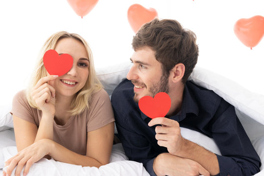 Close-up portrait of love couple attractive lovely girlish cheerful cheery girl holding in hands two heart symbol cards closing eyes on the bed. Holiday concept.