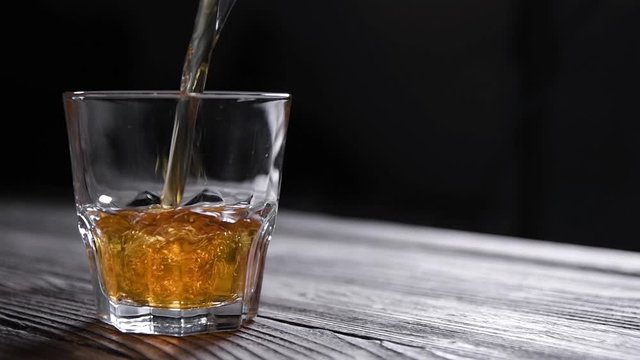 Whiskey is poured into a glass on a gray wooden table background. slow motion shot. front view