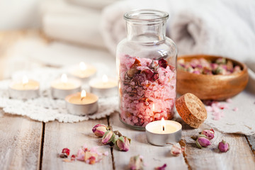 Fototapeta na wymiar Concept of spa treatment with roses. Crystals of sea pink salt in bottle, candles as decor. Atmosphere of relax and pleasure. Anti-stress and detox procedure. Luxury lifestyle. Wooden background