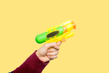 Concept of childhood, don't want to grow up, play with kids, play like a child. Hand of a young man holding a yellow and green toy gun. Yellow background