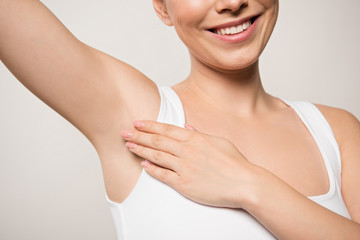 partial view of smiling woman applying deodorant on underarm isolated on grey - obrazy, fototapety, plakaty