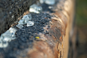 Fototapeta premium Small glass shards lying on a rusty peeling metal pipe. Shattered, broken glass fragments. Selective focus. Blurred background. Closeup view