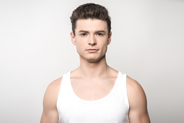 handsome man in white sleeveless shirt looking at camera isolated on grey