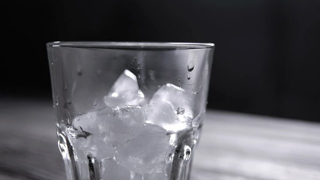  Throws ice and Whiskey poured into a glass with ice on a gray wooden table background. slow motion shot. front view