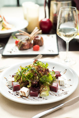 Fresh vegan salad with arugula, lettuce, beetroot, cheese and sauce on a white plate on a table in a restaurant. Close-up. Space