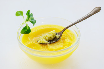 Ghee butter in a bowl with greens on a light table.