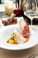 Traditional Caesar salad with chicken breast, tomatoes, lettuce, egg, parmesan and croutons in a white plate and a glass of white wine on a table in a restaurant. Close-up