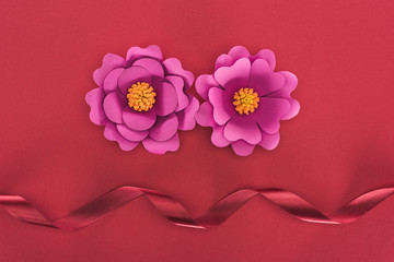 top view of paper pink paper flowers and red silk ribbon on red
