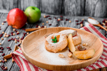 Apple donuts decorated with mint on round wooden plate on red striped napkin on gray wooden background