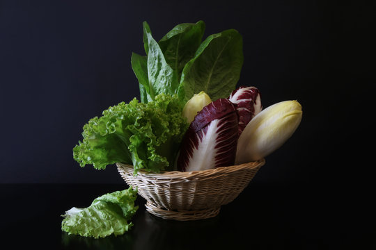 Cesto con insalata lattuga, cicoria, radicchio e indivia, su fondo nero