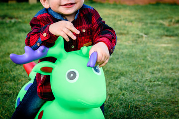 Child sitting on toy cow. Happy smiling child playing on grass.