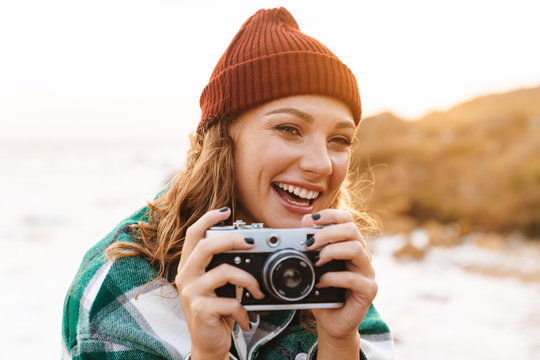 Image of caucasian woman taking photo on retro camera and laughing