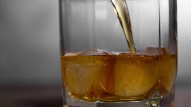  Throws ice and Whiskey poured into a glass with ice on a gray wooden table background. slow motion shot. front view