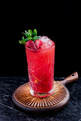 Beautiful red berry cocktail with ice, decorated with fresh berries and mint, on a round carved wooden board