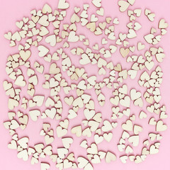 Background from many small wooden hearts on pink paper. Backdrop for wedding cards or Valentine. Top view. Flat lay.