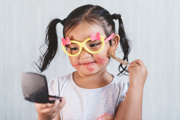 little asian girl playing with makeup blusher brush with dingy face. Concept of beauty and childhood