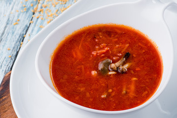 Red borsch of beets, vegetables and meat, with sour cream in white plate on blue rustic wooden background