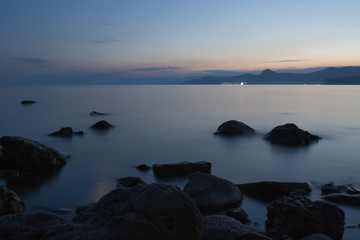 Sea at dusk. Stones on the shore and mountains in the distance.  Sea and mountains after sunset. Photo in the dark. Fog on the water.