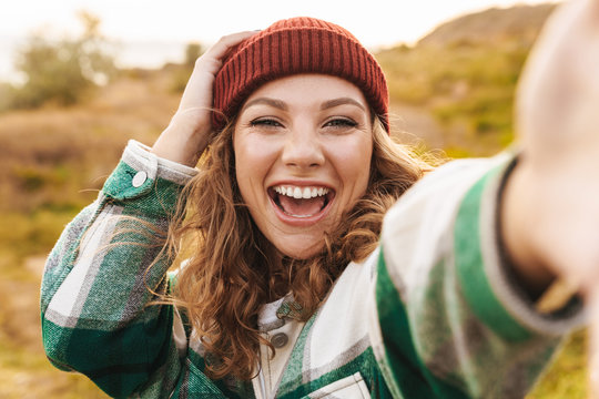Image of joyful young woman taking selfie photo while walking outdoors