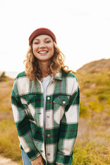 Image of young woman wearing hat and plaid shirt walking outdoors