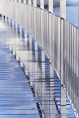 Reflection of chrome railing in the wet surface of the bridge after rain. Symmetric straight lines. Details of modern exterior design