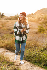 Image of joyful young woman holding cellphone while walking outdoors