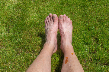 Elderly man's feet lying on a green lawn while resting after long bicycle trip