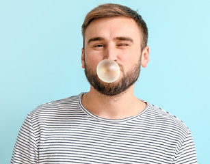 Funny man with chewing gum on color background