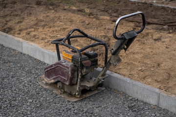 Vibrational paving stone machine for finish on a sidewalk road construction site.