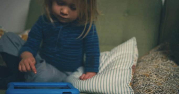 Little toddler using tablet computer on sofa next to his pregnant mother