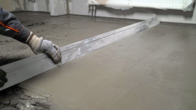 The process of leveling floors in the apartment with a solution. Construction work, concrete cement plaster. Using a spatula, level or level the concrete slab during the construction phase.