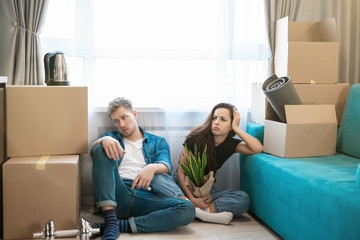 young couple man and woman looking tired sitting on the floor during moving to new appartment unpacking boxes, , moving process